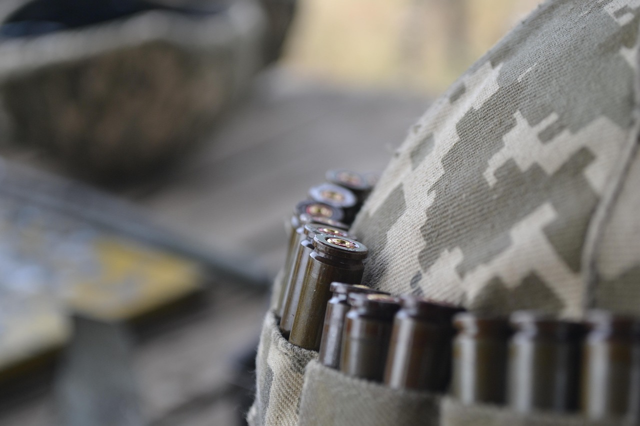 Bliskie ujęcie amunicji karabinowej umieszczonej w ładownicy na tle hełmu w kamuflażu cyfrowym.